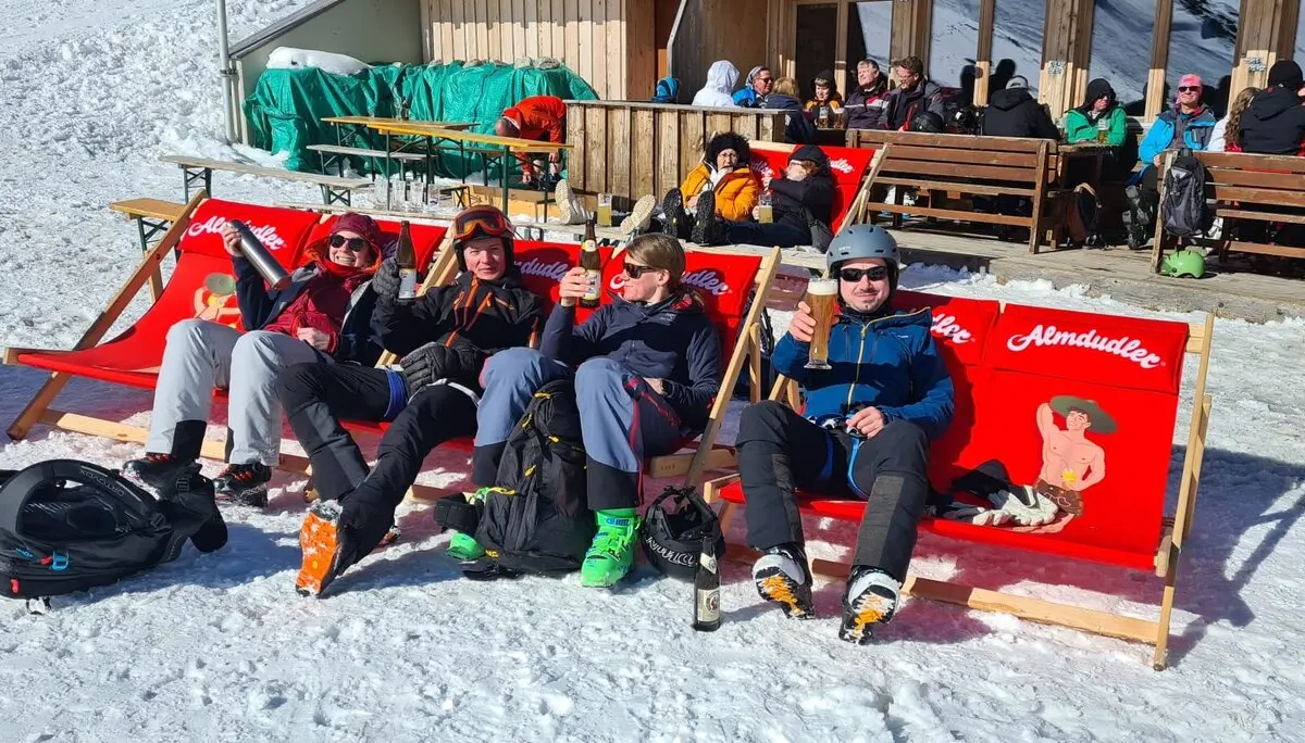 Vier Skifahrer*innen sitzen in roten Liegestühlen vor einer Skihütte und genießen die Sonne. | © DAV Dortmund