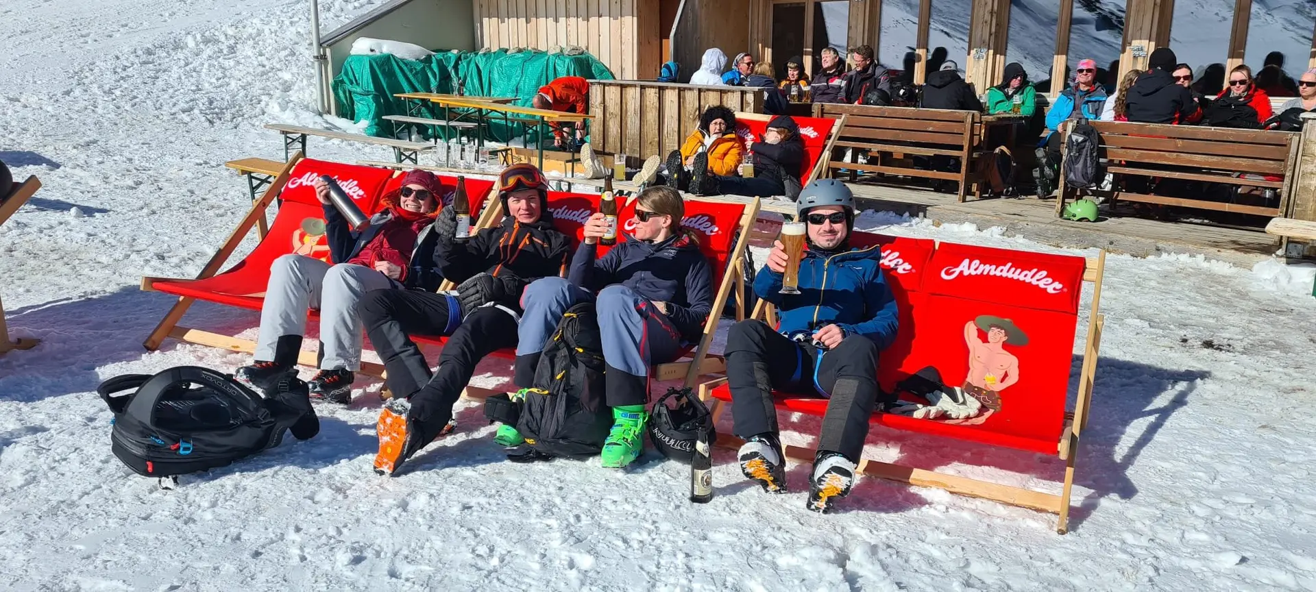 Vier Skifahrer*innen sitzen in roten Liegestühlen vor einer Skihütte und genießen die Sonne. | © DAV Dortmund