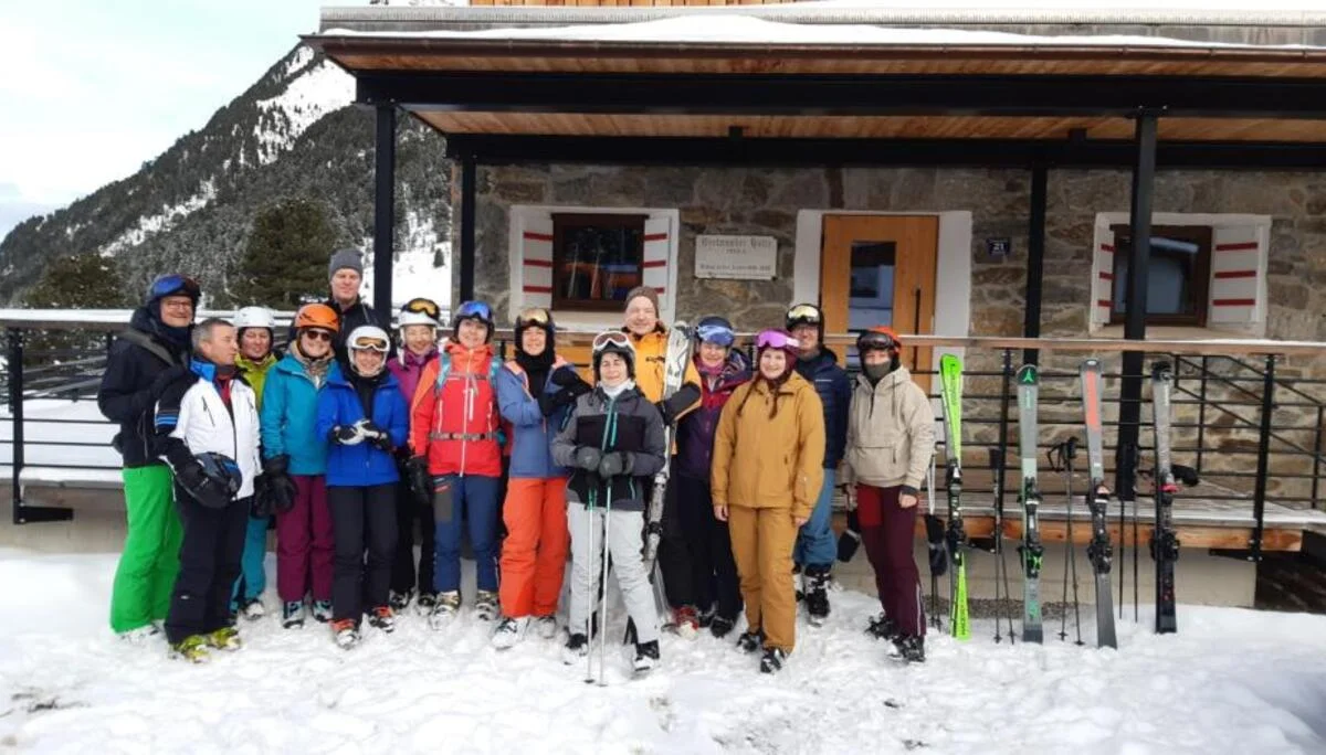 Eine große Skigruppe steht lächelnd vor einer verschneiten Berghütte mit Skiern im Schnee. | © DAV Dortmund
