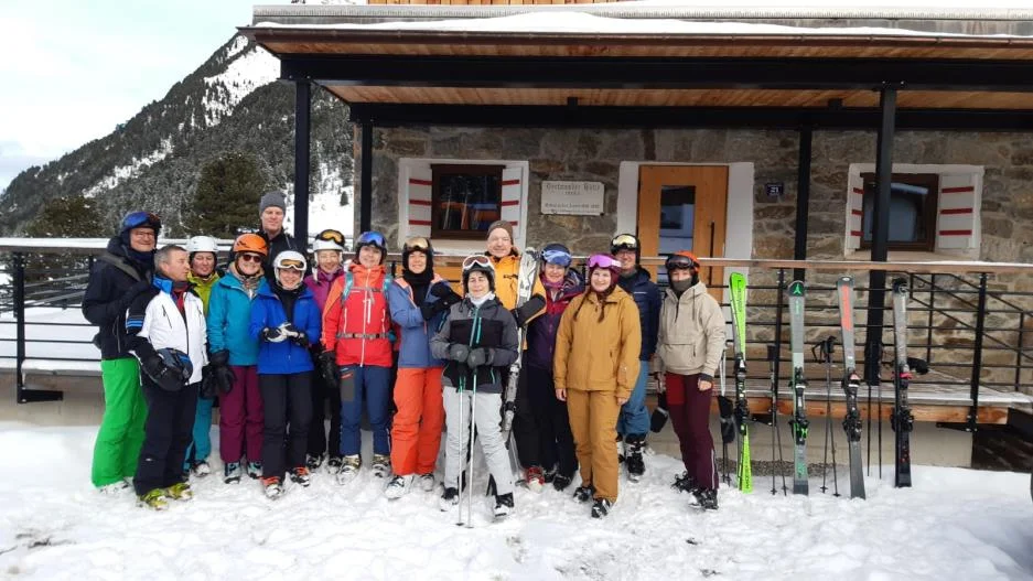 Eine große Skigruppe steht lächelnd vor einer verschneiten Berghütte mit Skiern im Schnee. | © DAV Dortmund