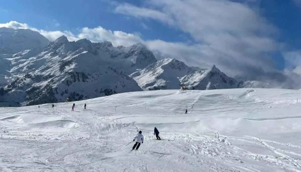Skifahrende in der Ferne auf einer großen, offenen Schneefläche mit Bergkulisse. | © DAV Dortmund