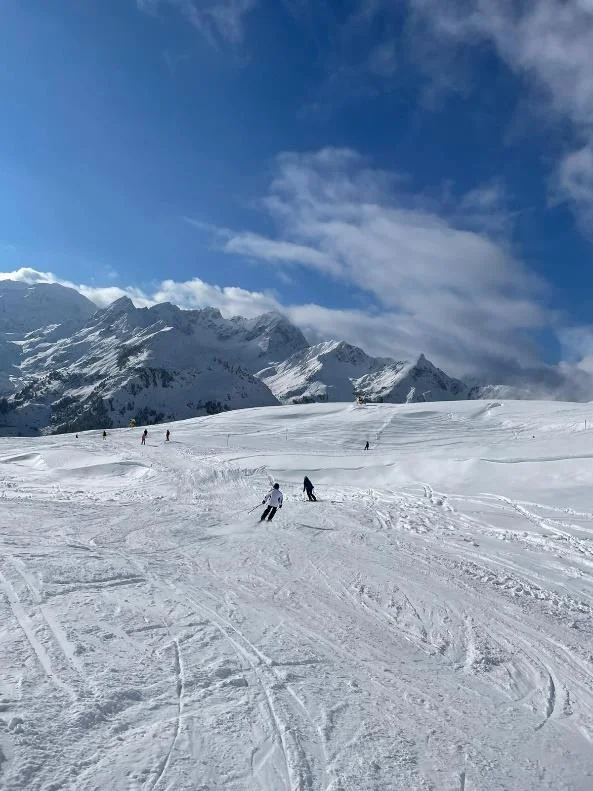 Skifahrende in der Ferne auf einer großen, offenen Schneefläche mit Bergkulisse. | © DAV Dortmund