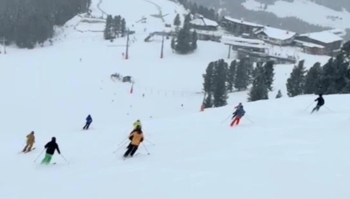 Mehrere Skifahrende fahren eine breite Piste mit Blick auf ein Skigebiet hinab. | © DAV Dortmund