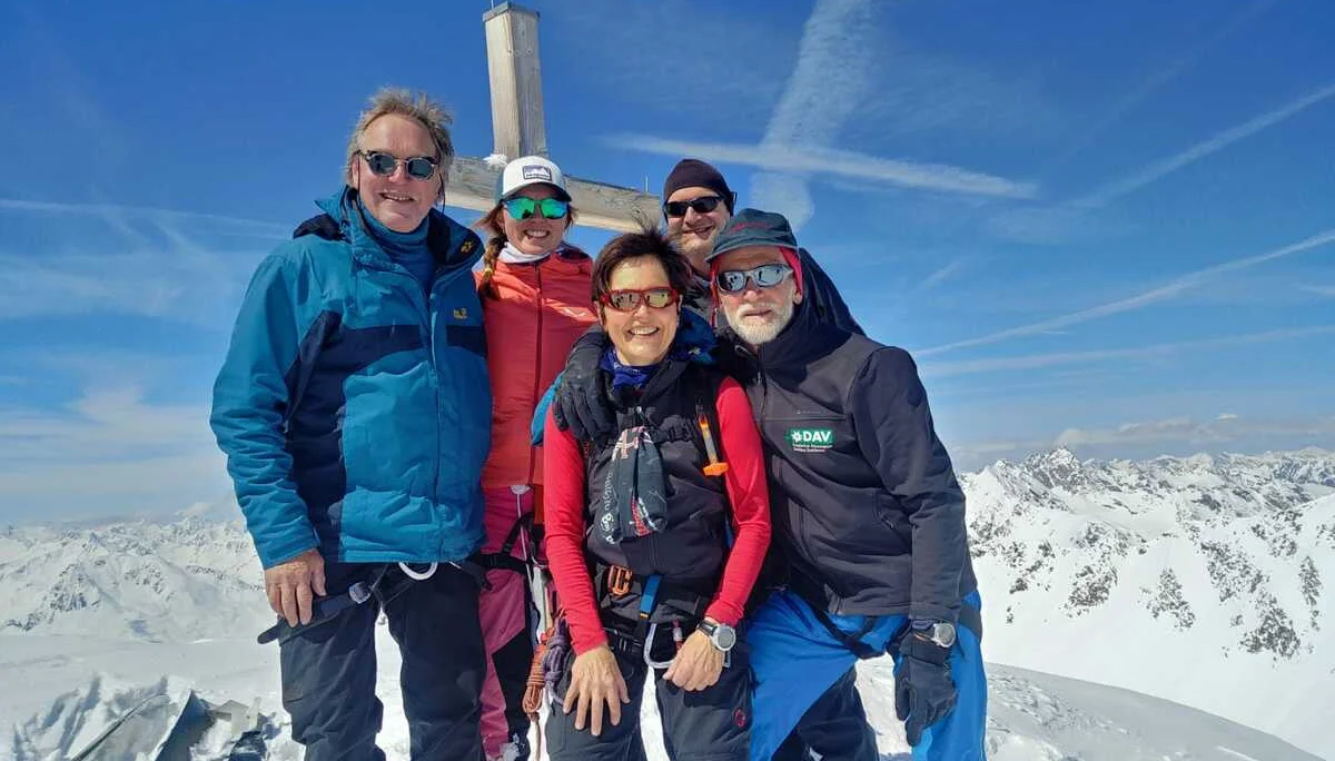 Fünf Personen stehen bei klarem Himmel vor einem Holzkreuz auf einem Gipfel inmitten der Alpen. | © DAV Dortmund