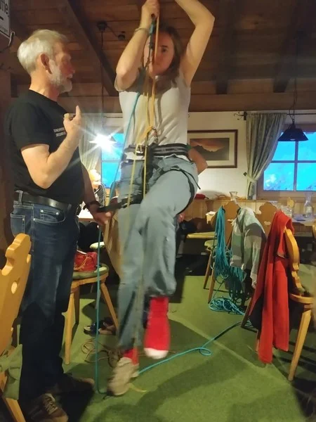 Eine Frau übt das Aufsteigen am Seil mit Unterstützung eines Trainers in einem gemütlichen Seminarraum. | © DAV Dortmund