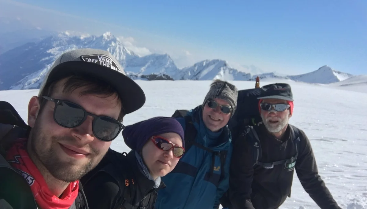 Vier Personen lachen in die Kamera mit verschneiten Gipfeln im Hintergrund. | © DAV Dortmund