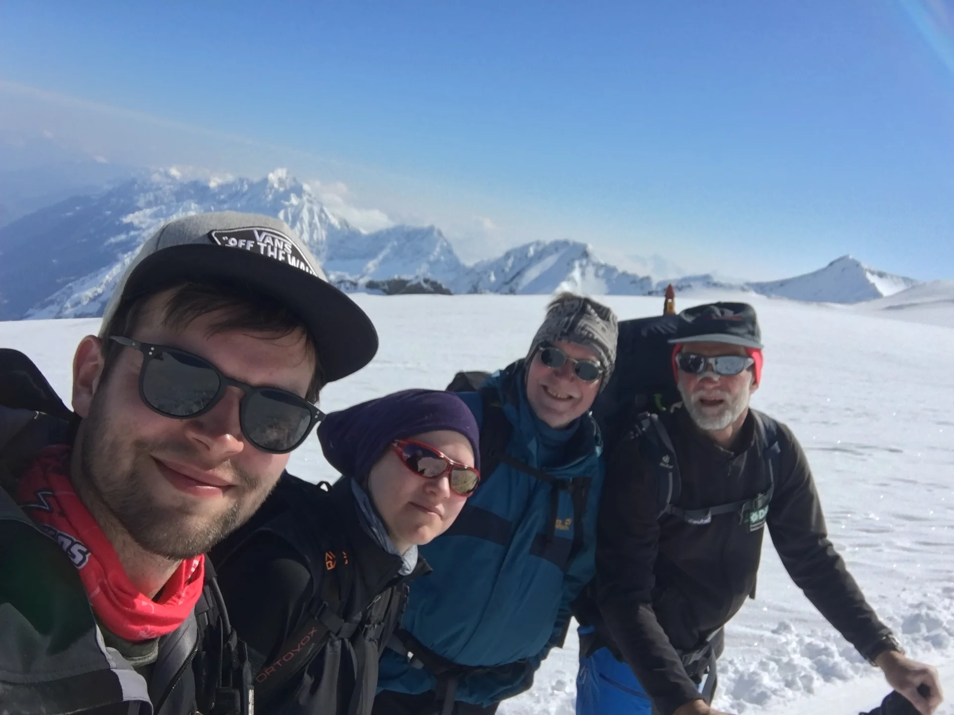 Vier Personen lachen in die Kamera mit verschneiten Gipfeln im Hintergrund. | © DAV Dortmund