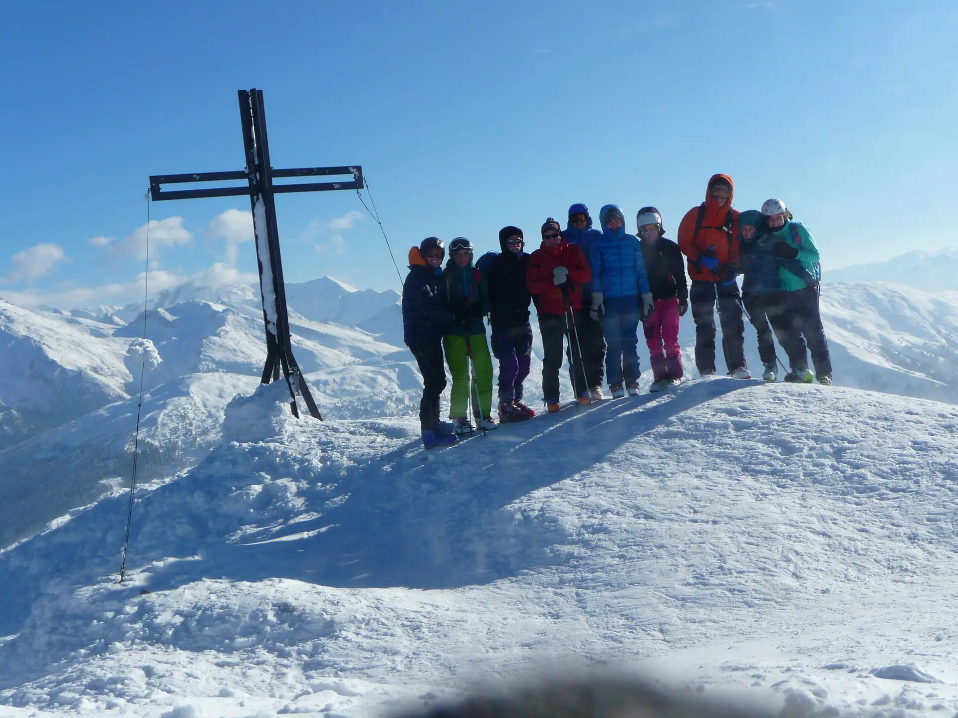 Jugendliche in bunter Winterkleidung stehen auf einem verschneiten Gipfel mit schwarzem Gipfelkreuz. | © DAV Dortmund