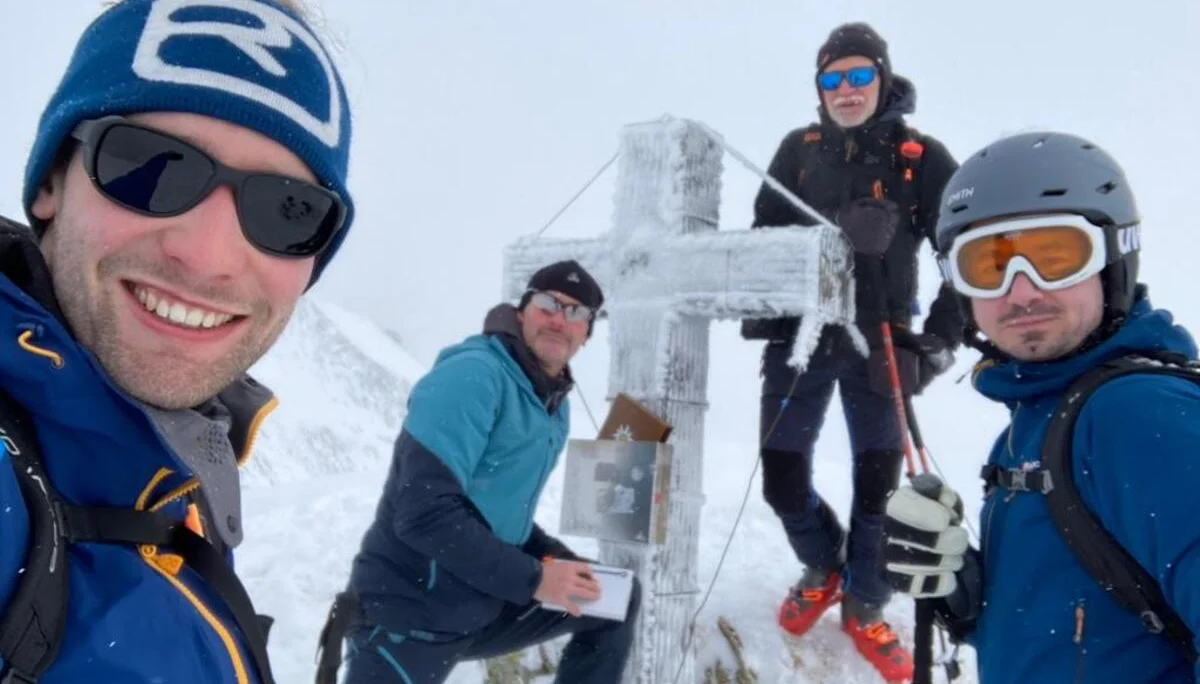 Vier Skibergsteiger posieren an einem mit Eis bedeckten Gipfelkreuz bei Schneefall. | © DAV Dortmund