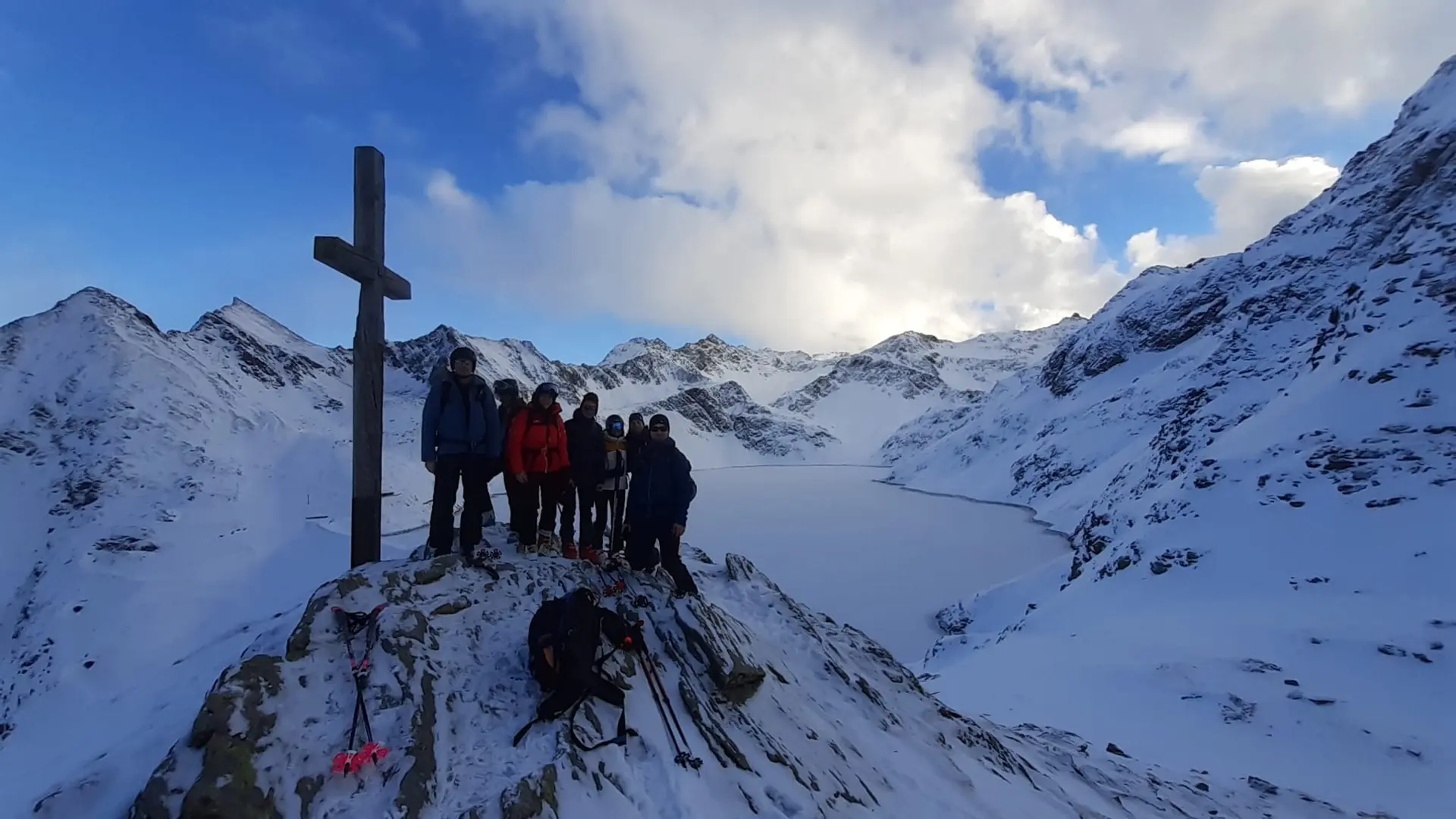Gruppe steht am Gipfelkreuz mit Blick auf einen gefrorenen See inmitten schneebedeckter Berge. | © DAV Dortmund