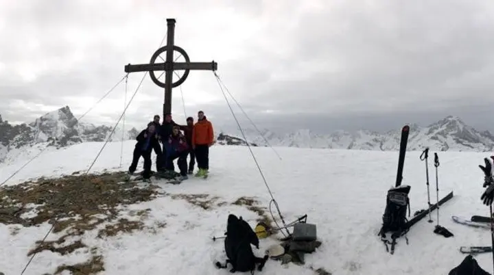 Fünf Skitourengeher*innen posieren am Gipfelkreuz mit Blick auf schneebedeckte Berge. | © DAV Dortmund