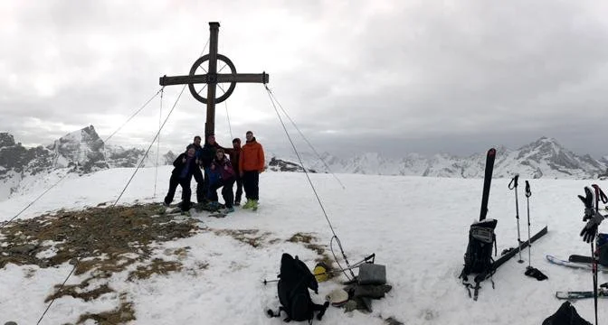 Fünf Skitourengeher*innen posieren am Gipfelkreuz mit Blick auf schneebedeckte Berge. | © DAV Dortmund