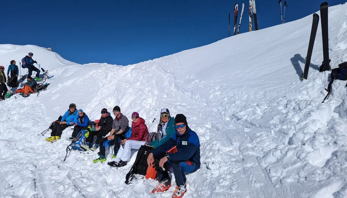 Sieben Personen machen bei Sonnenschein eine Pause im Schnee, Skier stehen neben ihnen im Hang. | © DAV Dortmund
