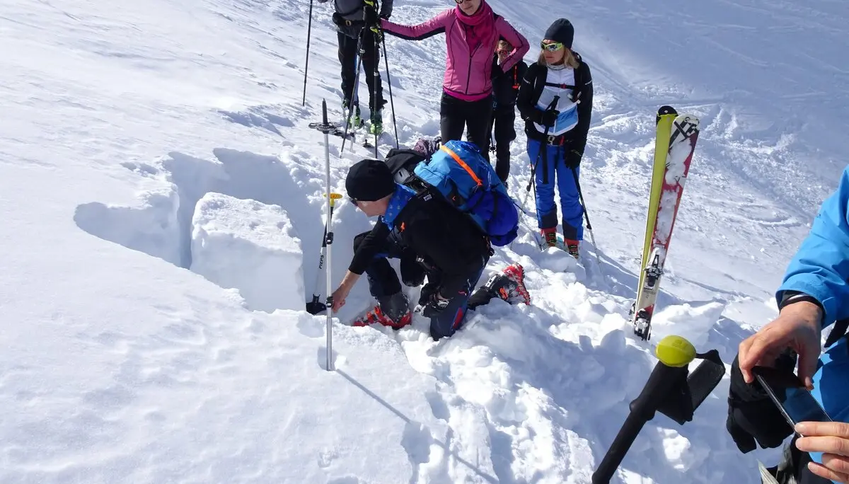 Eine Gruppe beobachtet eine Person, die ein Schneeprofil im Tiefschnee für eine Lawinenbeurteilung gräbt. | © DAV Dortmund