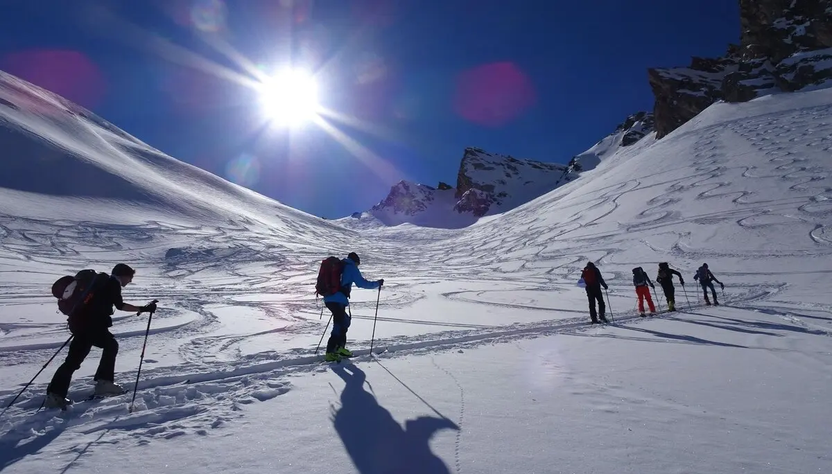 Eine Gruppe von Skitourengeher*innen steigt bei Sonne über einen unberührten Schneehang mit Spuren im Hintergrund. | © DAV Dortmund