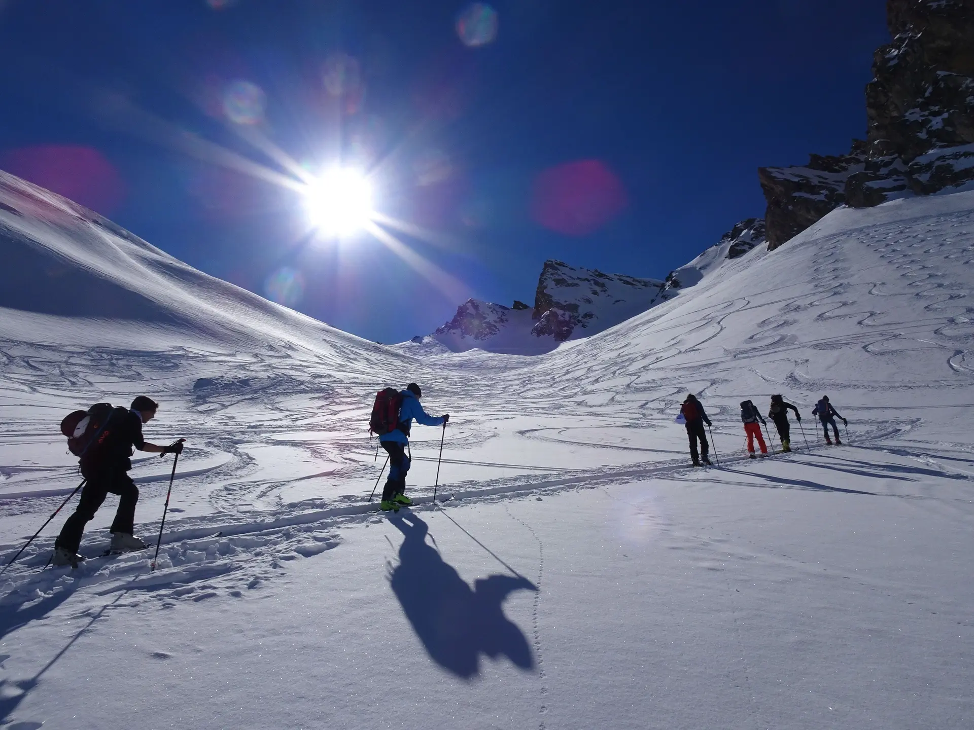 Eine Gruppe von Skitourengeher*innen steigt bei Sonne über einen unberührten Schneehang mit Spuren im Hintergrund. | © DAV Dortmund