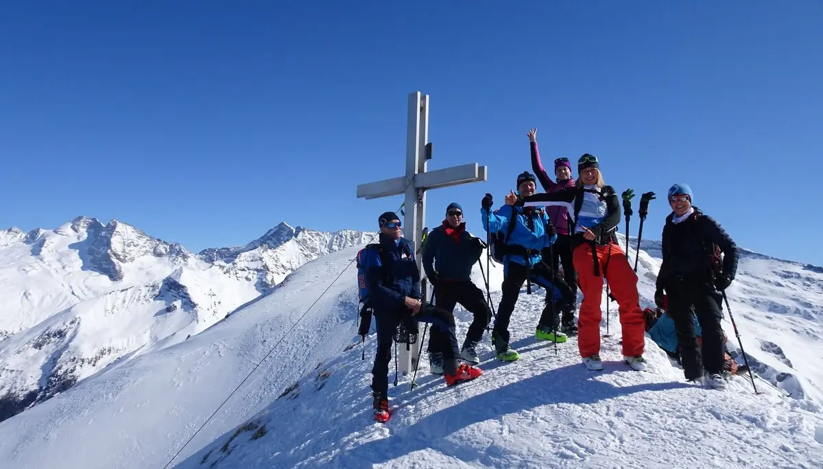 Sechs Personen mit Skiern feiern bei strahlendem Sonnenschein am verschneiten Gipfelkreuz. | © DAV Dortmund