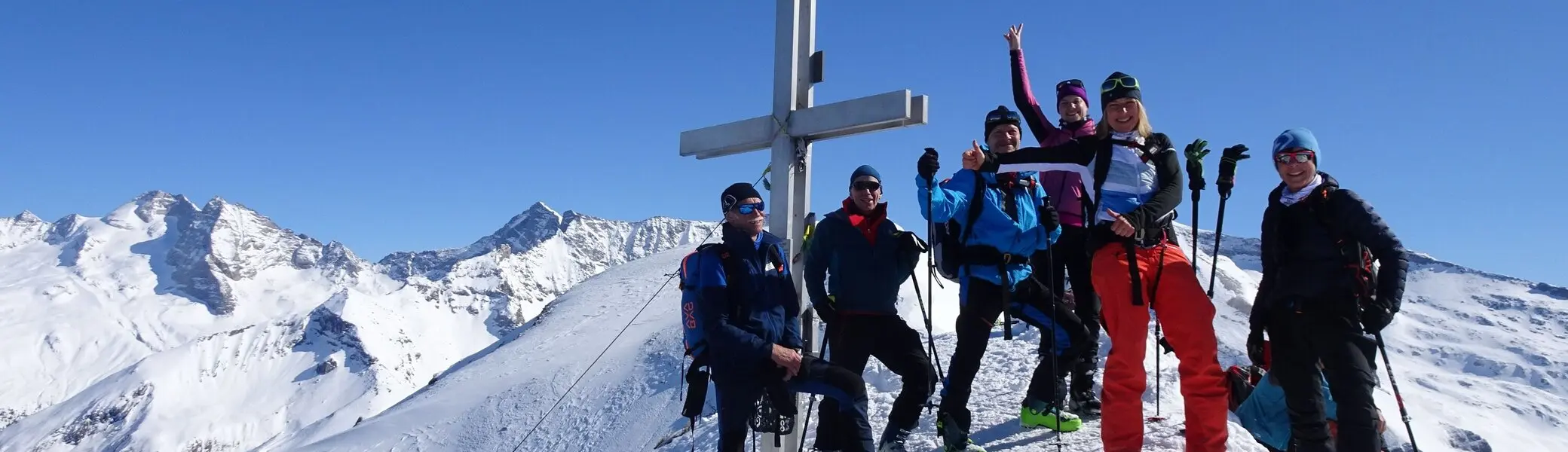 Sechs Personen mit Skiern feiern bei strahlendem Sonnenschein am verschneiten Gipfelkreuz. | © DAV Dortmund