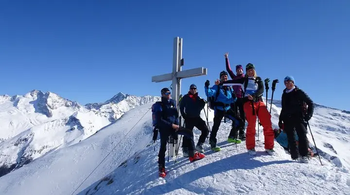 Sechs Personen mit Skiern feiern bei strahlendem Sonnenschein am verschneiten Gipfelkreuz. | © DAV Dortmund