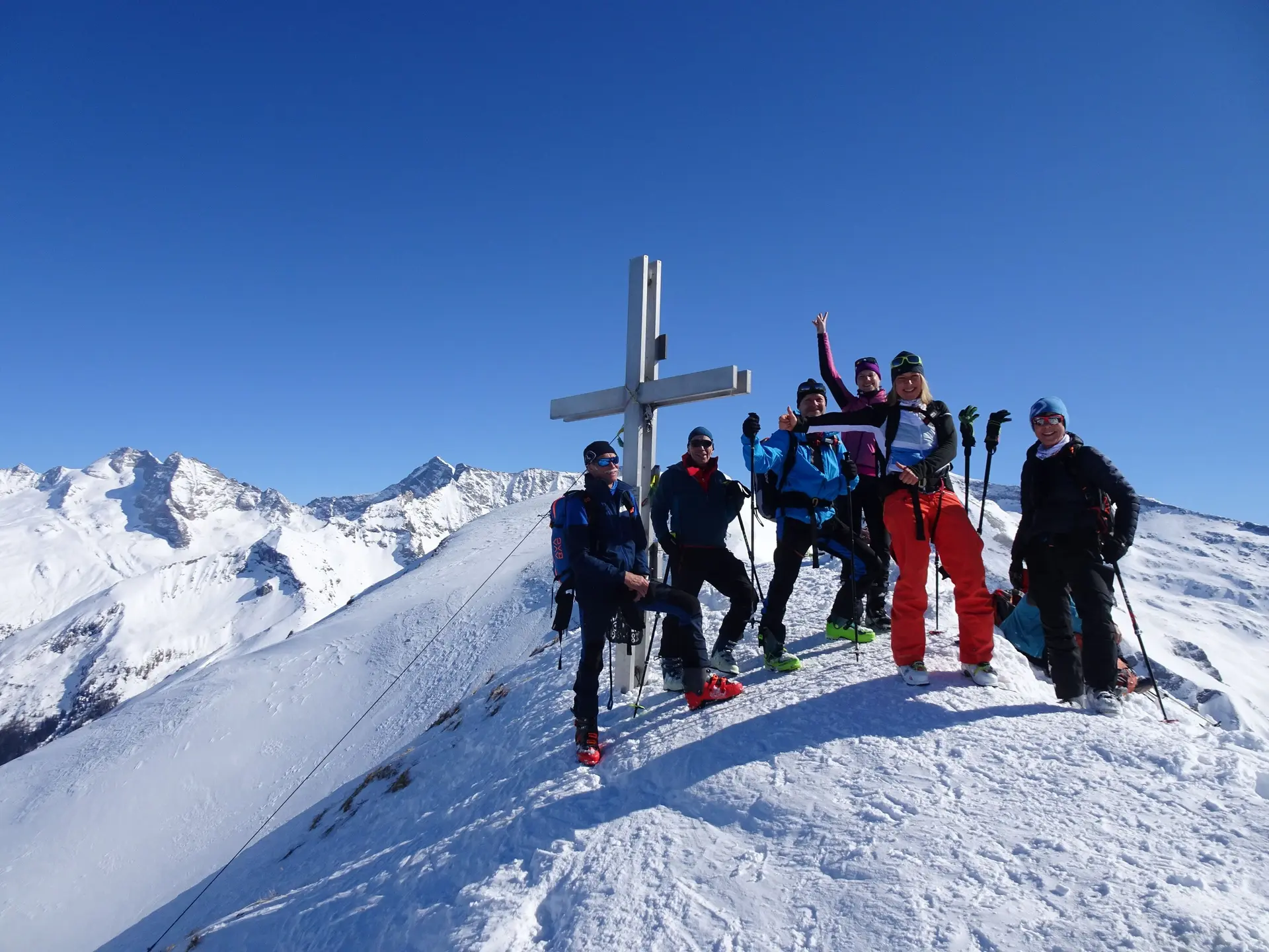 Sechs Personen mit Skiern feiern bei strahlendem Sonnenschein am verschneiten Gipfelkreuz. | © DAV Dortmund