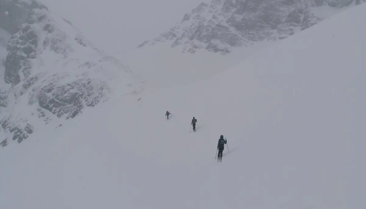 Vier Personen gehen in weiter Ferne durch eine verschneite Mulde zwischen zwei Bergrücken. | © DAV Dortmund