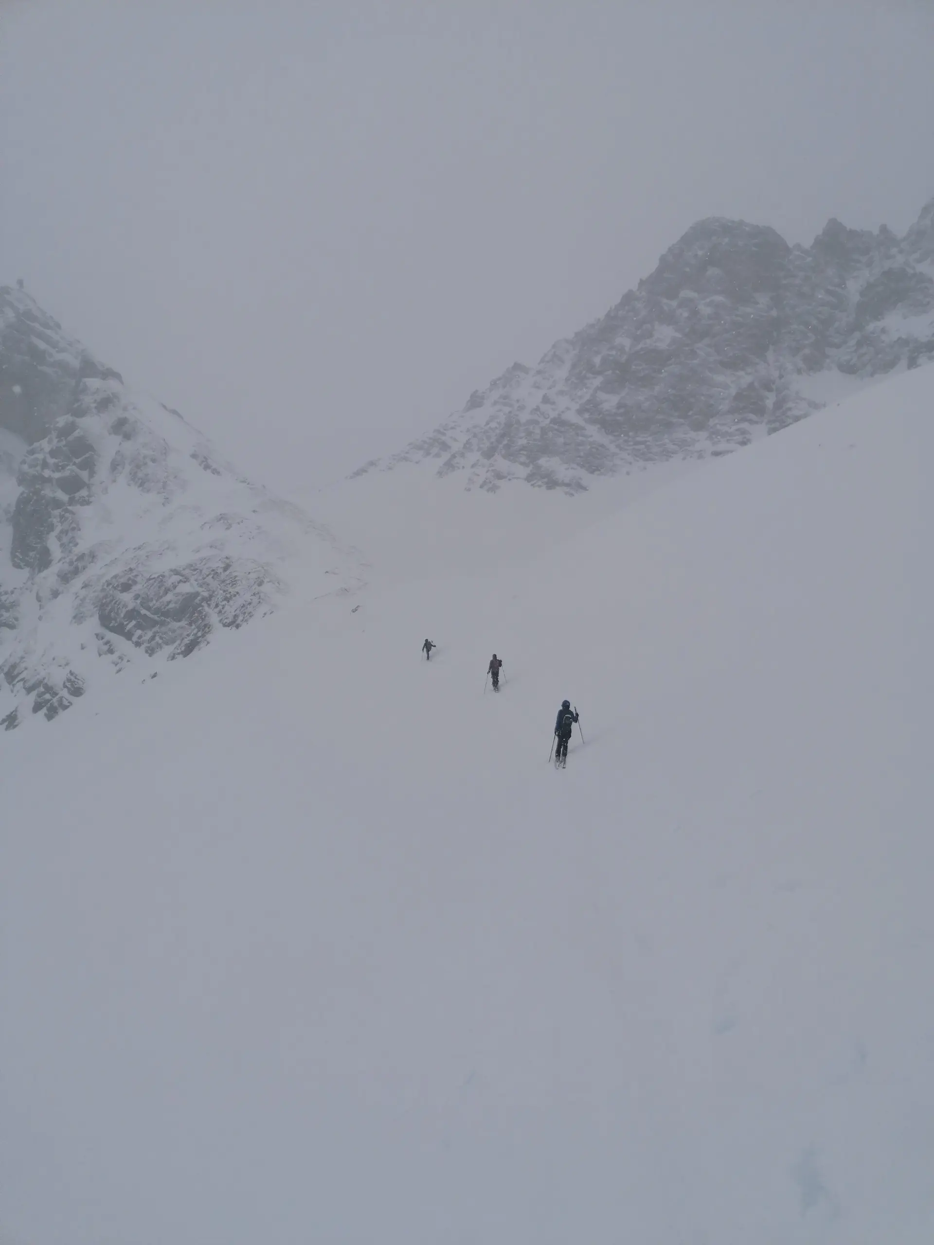 Vier Personen gehen in weiter Ferne durch eine verschneite Mulde zwischen zwei Bergrücken. | © DAV Dortmund