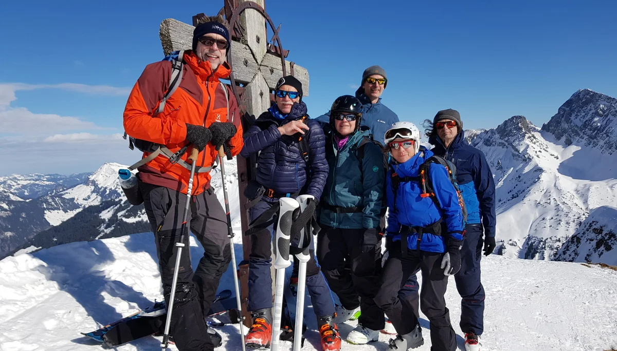 Eine Gruppe posiert am Gipfelkreuz bei Sonnenschein und winterlicher Aussicht. | © DAV Dortmund