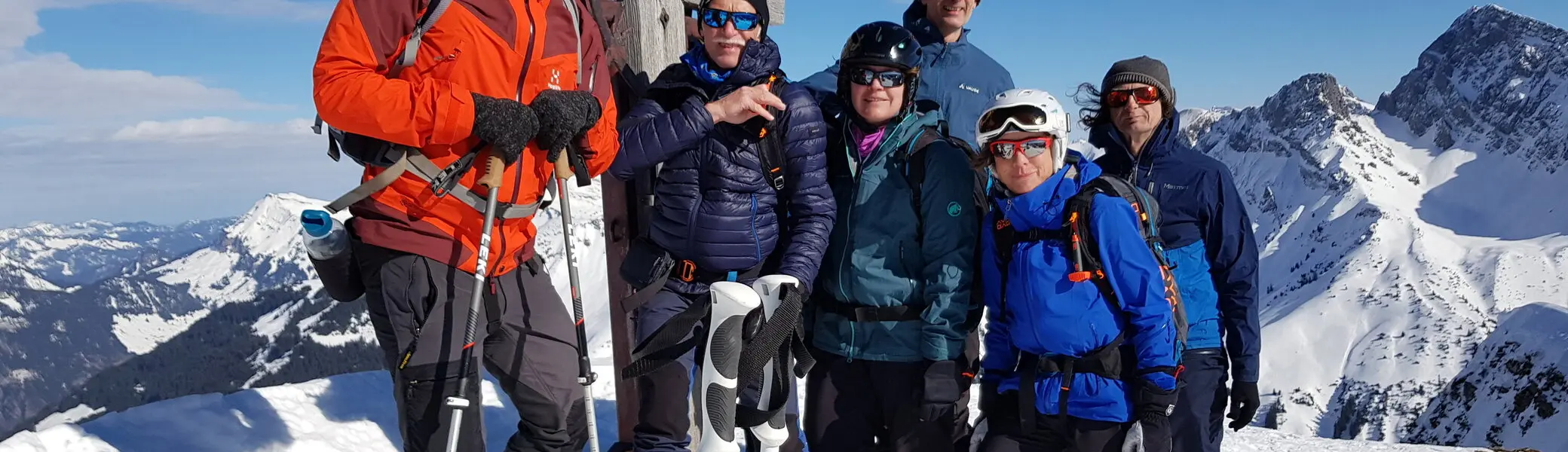 Eine Gruppe posiert am Gipfelkreuz bei Sonnenschein und winterlicher Aussicht. | © DAV Dortmund