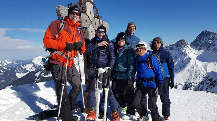 Eine Gruppe posiert am Gipfelkreuz bei Sonnenschein und winterlicher Aussicht. | © DAV Dortmund