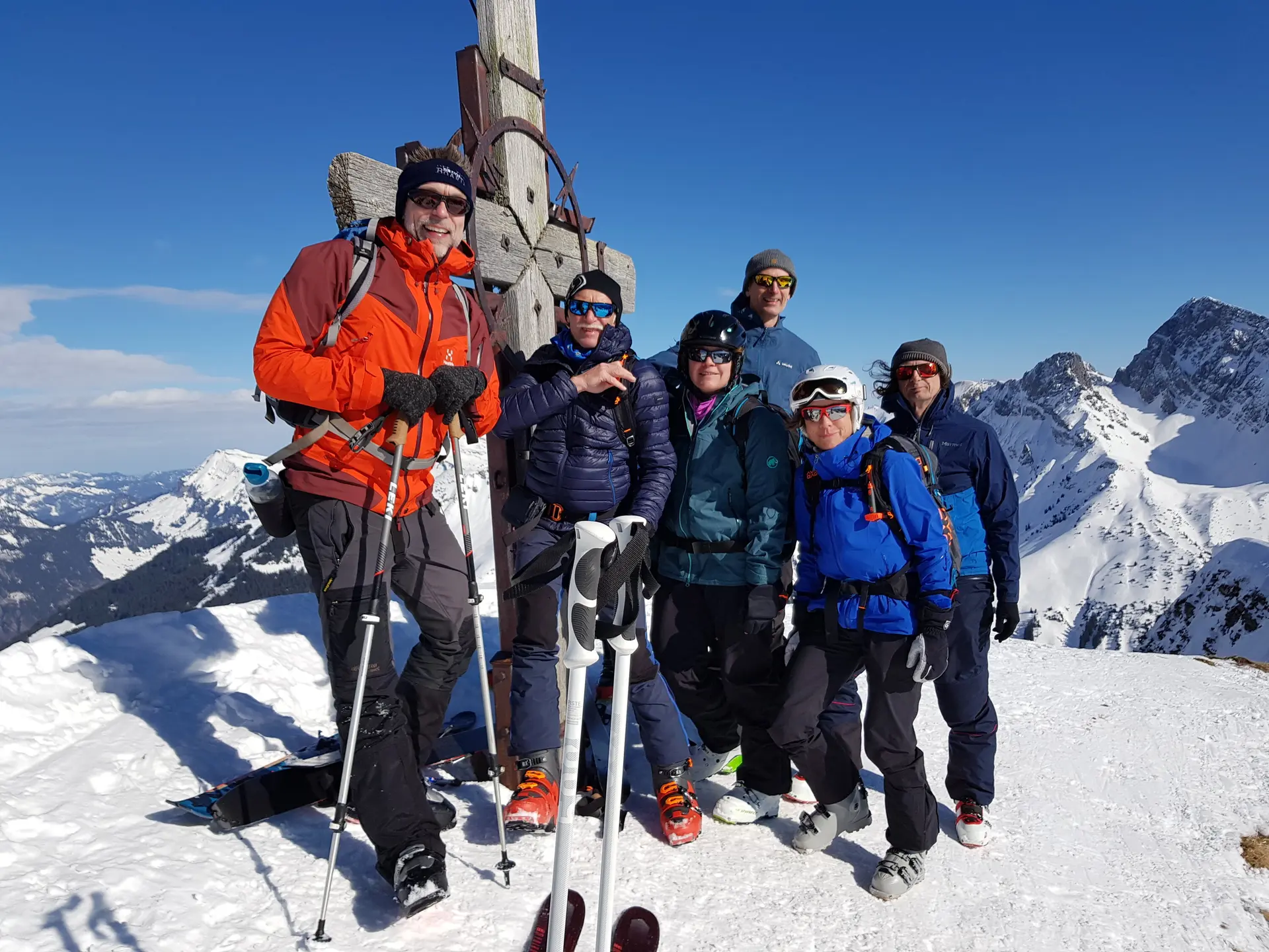 Eine Gruppe posiert am Gipfelkreuz bei Sonnenschein und winterlicher Aussicht. | © DAV Dortmund