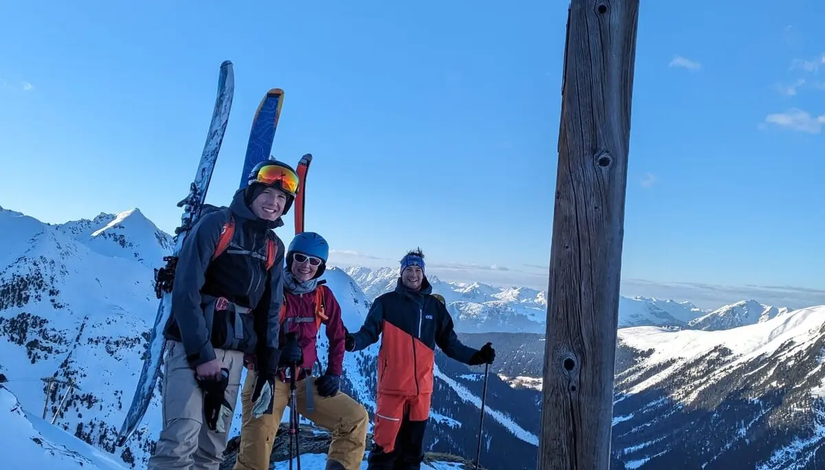 Drei Skitourengeher*innen stehen auf einem verschneiten Gipfel mit Holzkreuz. | © DAV Dortmund