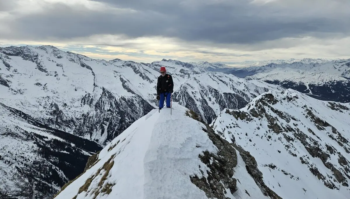 Person steht allein auf einem schmalen, verschneiten Grat mit Weitblick über ein Bergpanorama. | © DAV Dortmund