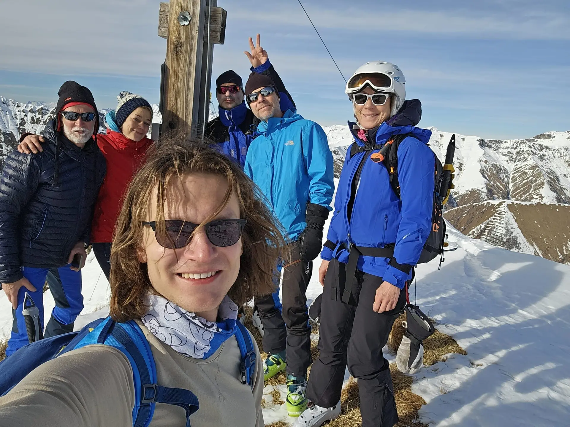 Sechs Skitourengeher*innen machen ein Selfie an einem Gipfelkreuz bei Sonnenschein. | © DAV Dortmund