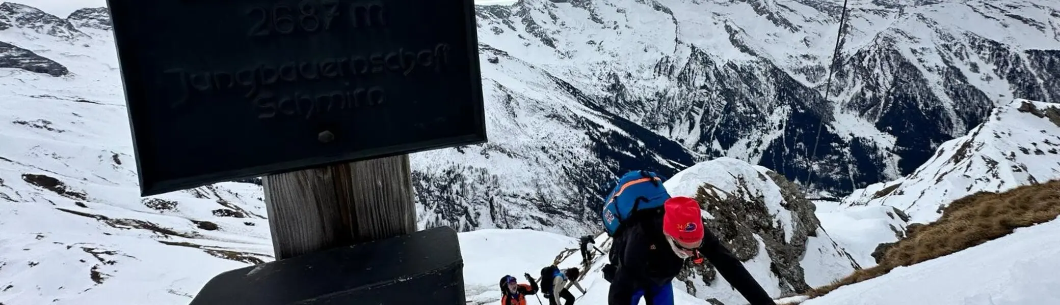 Gruppe von Skitourengeher*innen beim steilen Aufstieg am Hochschober, Gipfelschild im Vordergrund. | © DAV Dortmund
