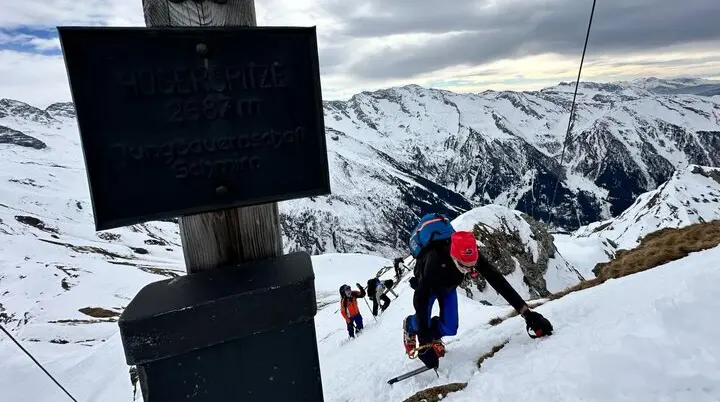 Gruppe von Skitourengeher*innen beim steilen Aufstieg am Hochschober, Gipfelschild im Vordergrund. | © DAV Dortmund