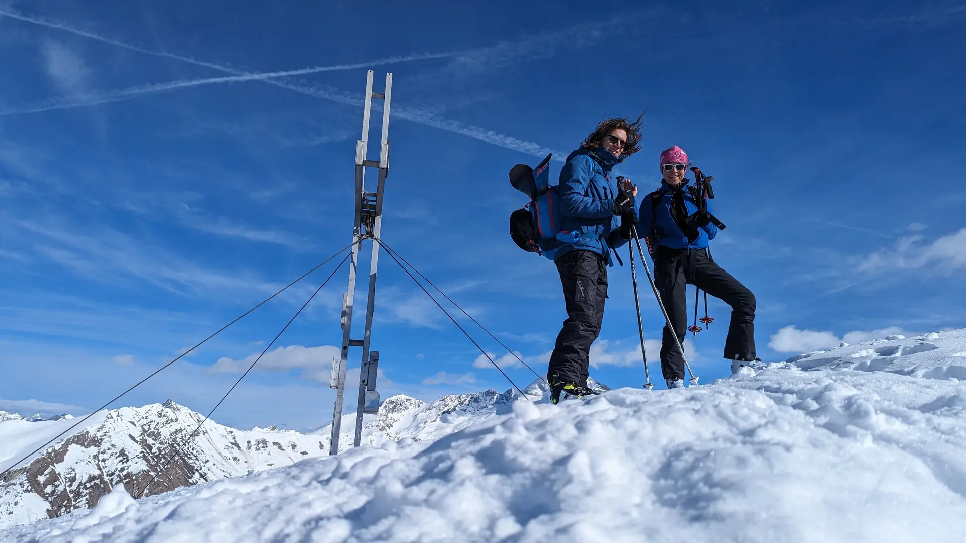 Zwei Skitourengeher*innen stehen am Gipfel mit großem Kreuz, blauer Himmel im Hintergrund. | © DAV Dortmund