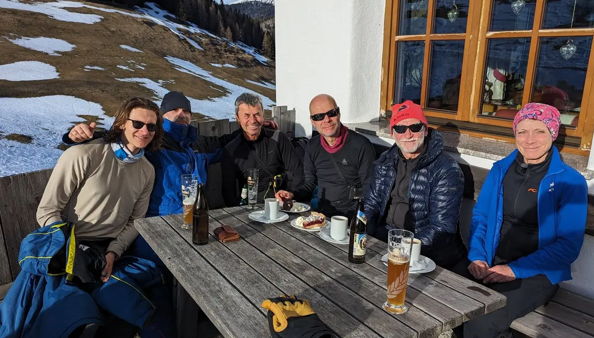 Sechs Personen sitzen an einem Holztisch vor einer Hütte, genießen Getränke und Kuchen. | © DAV Dortmund