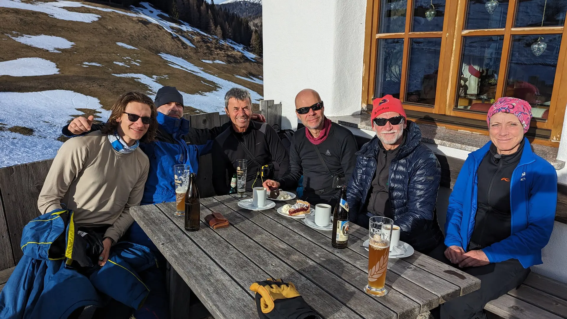 Sechs Personen sitzen an einem Holztisch vor einer Hütte, genießen Getränke und Kuchen. | © DAV Dortmund