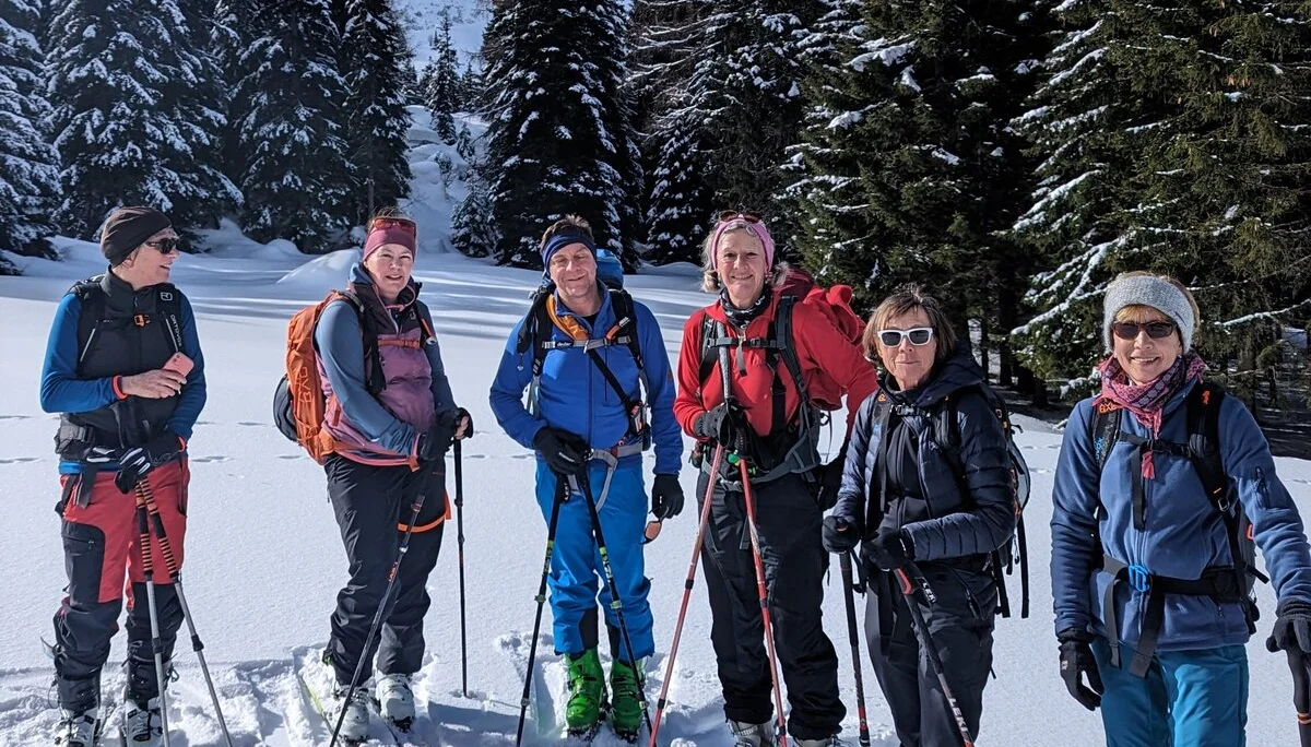 Sechs Skitourengeher*innen posieren lachend im verschneiten Wald bei blauem Himmel. | © DAV Dortmund