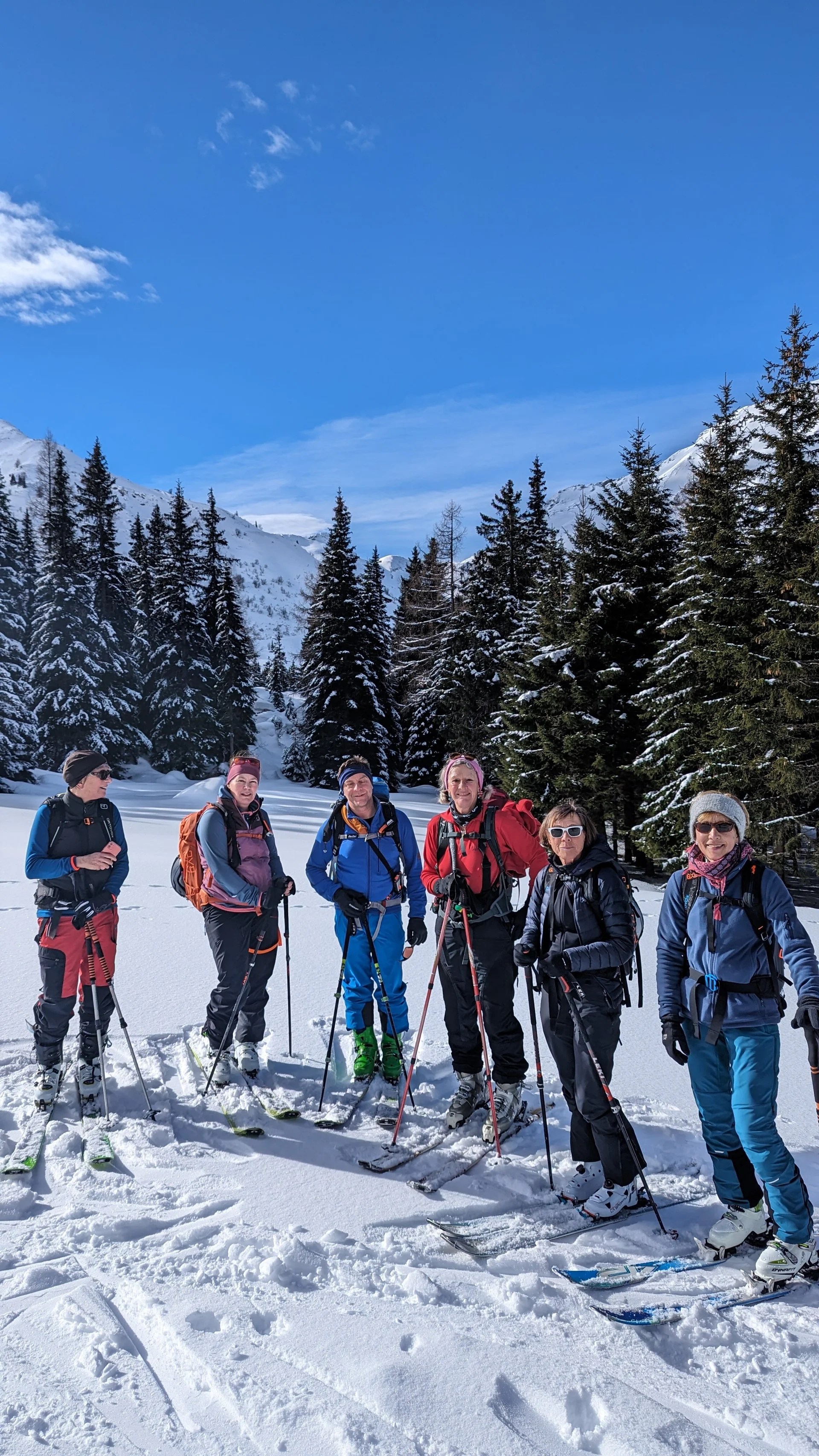 Sechs Skitourengeher*innen posieren lachend im verschneiten Wald bei blauem Himmel. | © DAV Dortmund