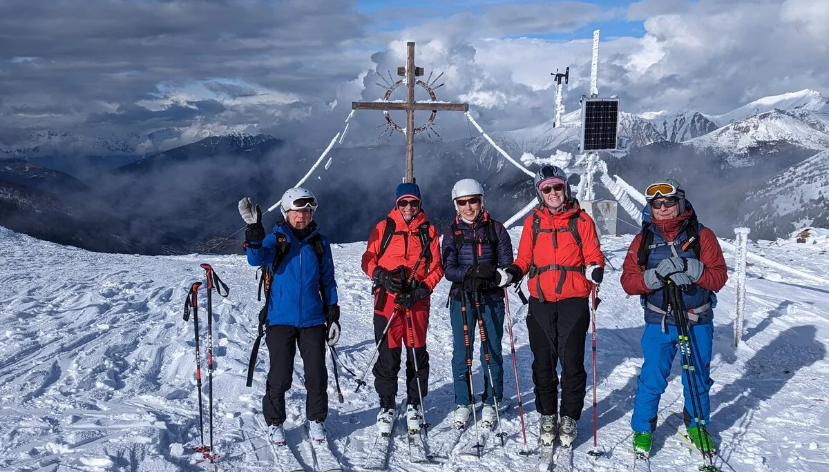 Fünf Skitourengeher*innen stehen vor einem Gipfelkreuz mit bewölktem Himmel im Hintergrund. | © DAV Dortmund