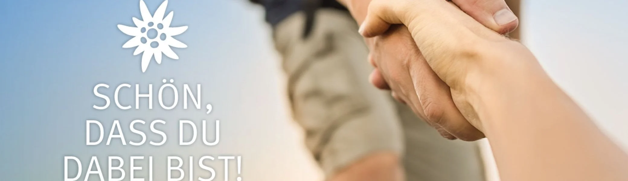 Zwei Hände greifen sich, im Hintergrund eine wandernde Person. Text mit Edelweiß: „Schön, dass du dabei bist!“ | © kieferpix