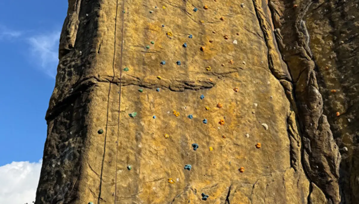 Der frisch sanierte Kletterturm in Dortmund mit deutlich sichtbaren neuen Griffen in verschiedenen Farben. Einzelne Routenzettel sind an der Wand befestigt, ein Seil hängt von oben herab. | © DAV Dortmund