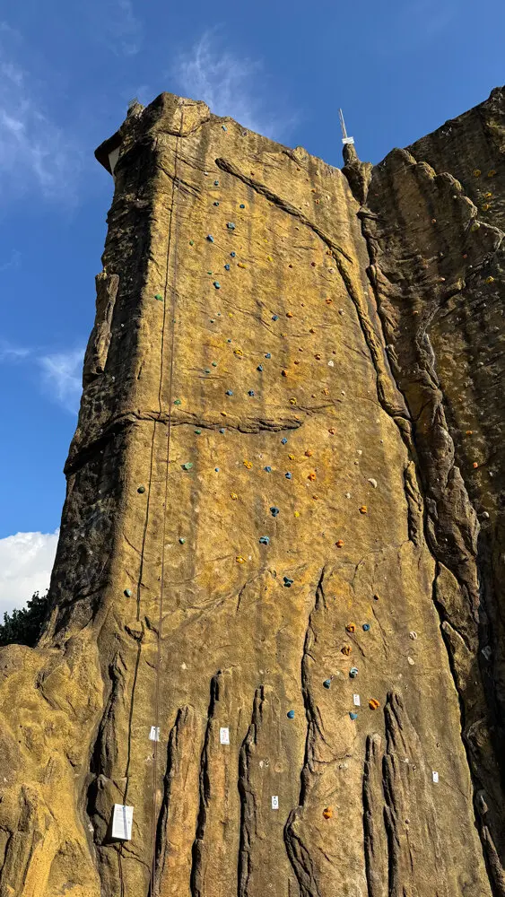 Der frisch sanierte Kletterturm in Dortmund mit deutlich sichtbaren neuen Griffen in verschiedenen Farben. Einzelne Routenzettel sind an der Wand befestigt, ein Seil hängt von oben herab. | © DAV Dortmund