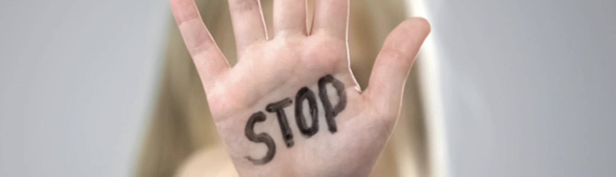Hand mit aufgeschriebenem Wort „STOP“, im Hintergrund eine Frau. Symbol für Schutz und Prävention. | © DAV Dortmund