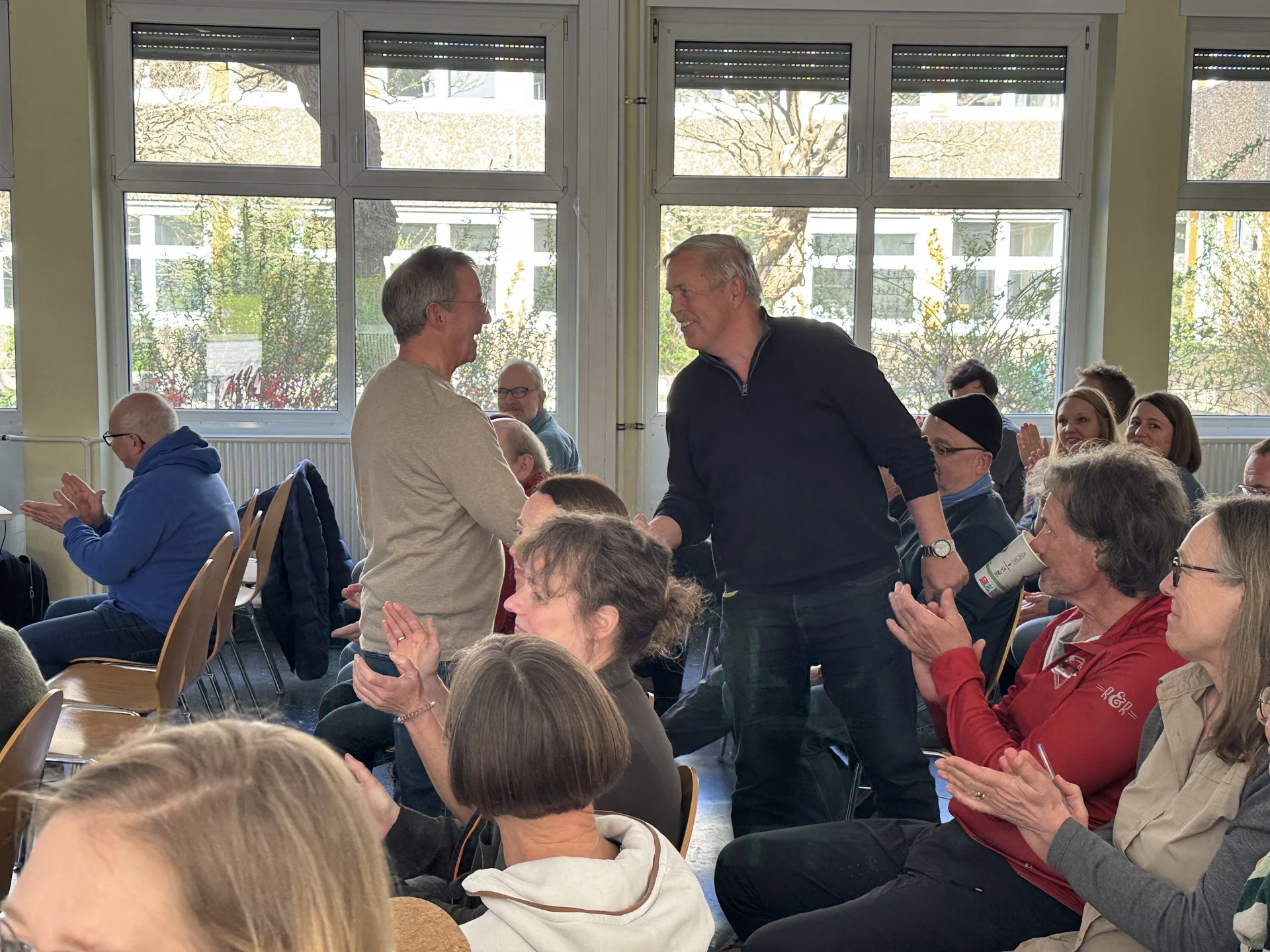 Zwei Männer stehen inmitten einer applaudierenden Gruppe in einem Veranstaltungsraum. | © DAV Dortmund