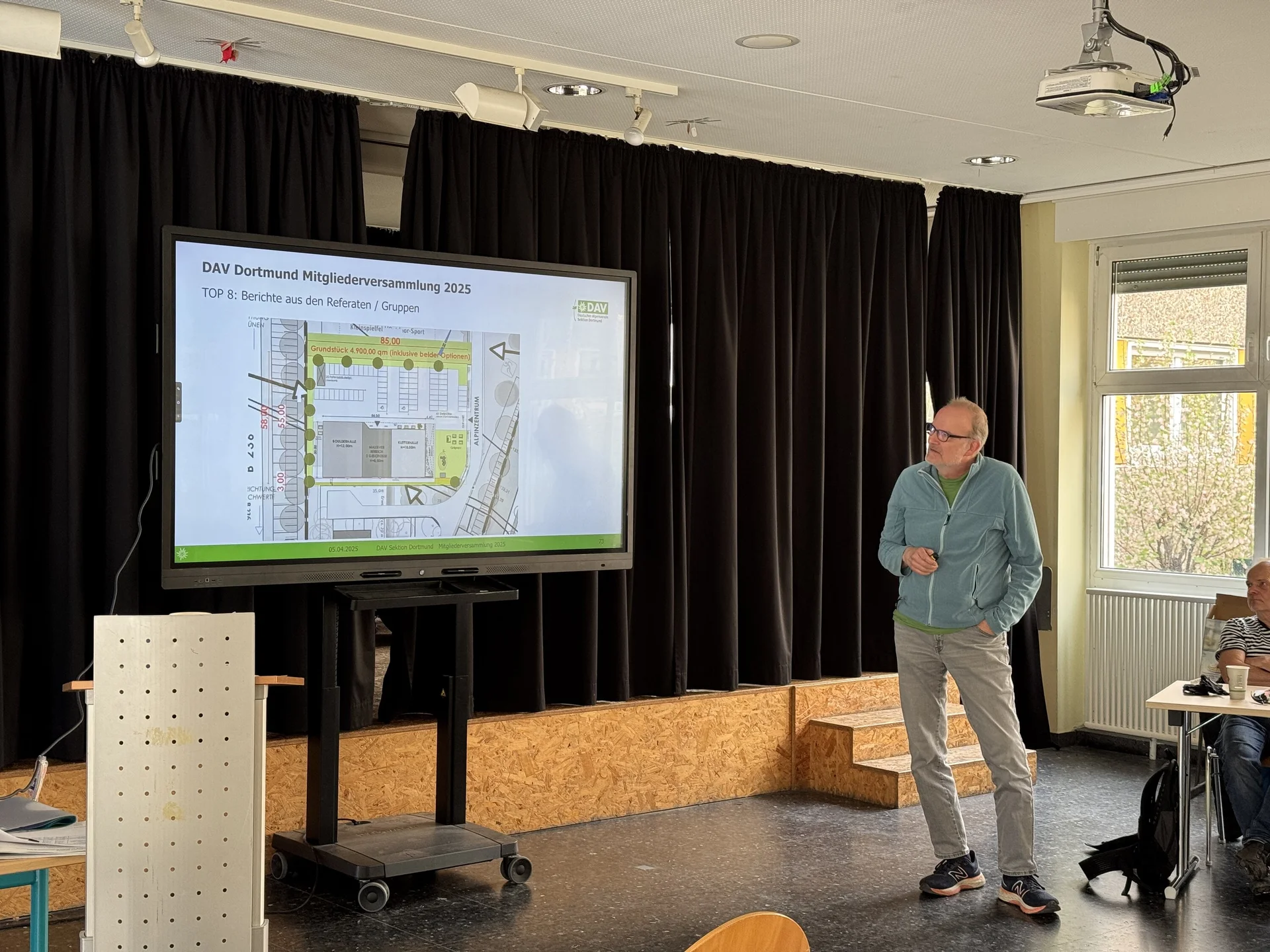 Ein Mann präsentiert einen Bauplan des DAV-Zentrums auf einer großen Leinwand während der Mitgliederversammlung. | © DAV Dortmund