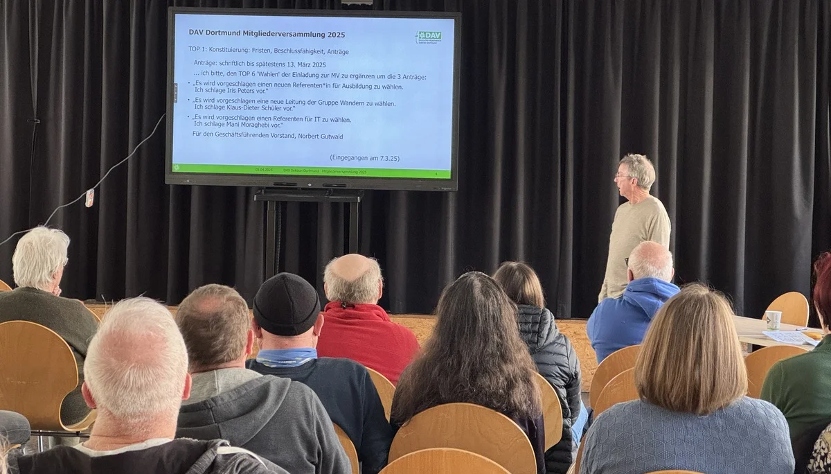 Ein Mann steht vor einer Leinwand mit einer Präsentation über Tagesordnungspunkte bei der DAV Mitgliederversammlung. | © DAV Dortmund