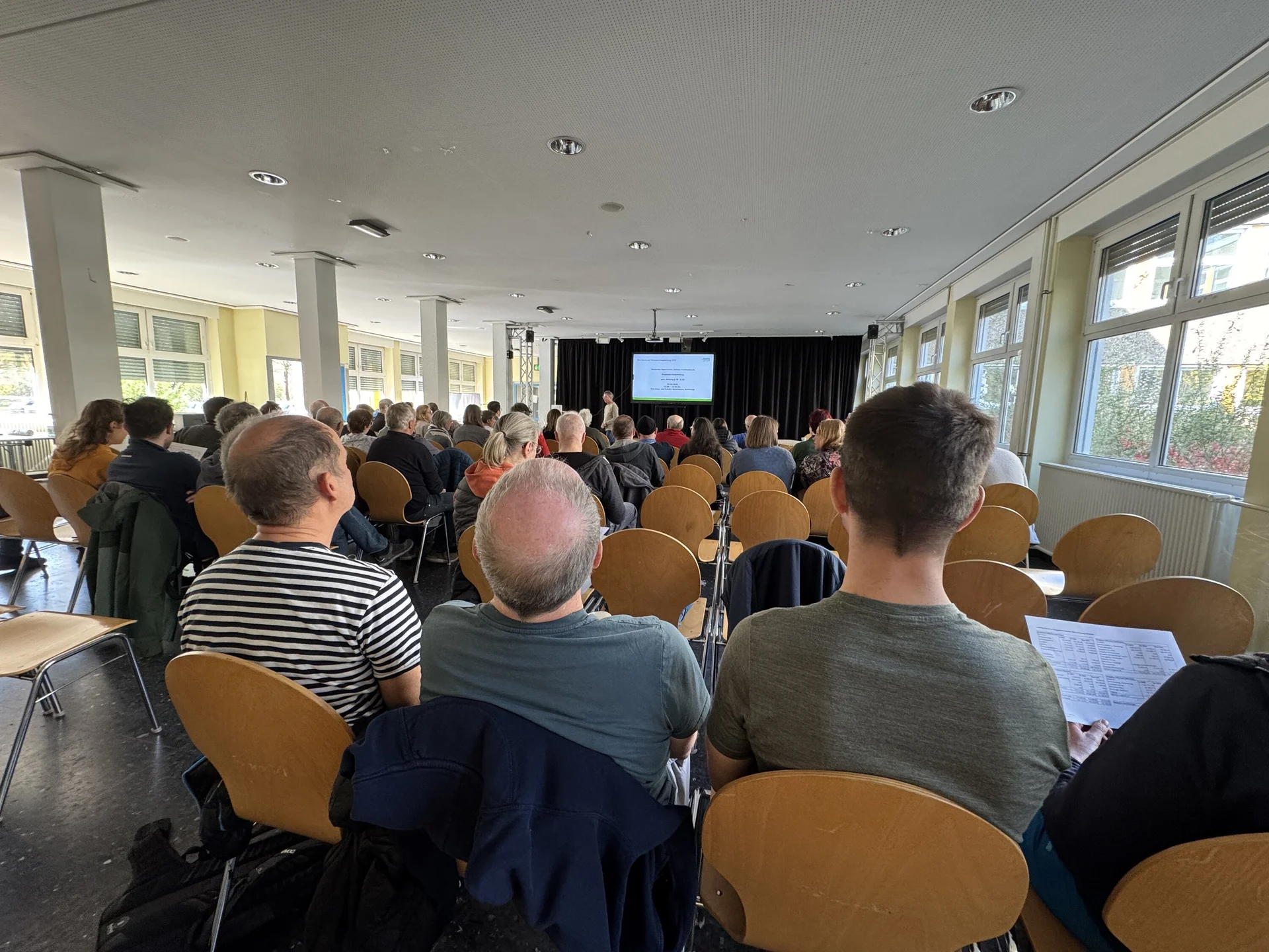 Viele Teilnehmer*innen sitzen in einem großen, hellen Saal und verfolgen eine Präsentation auf der Bühne. | © DAV Dortmund