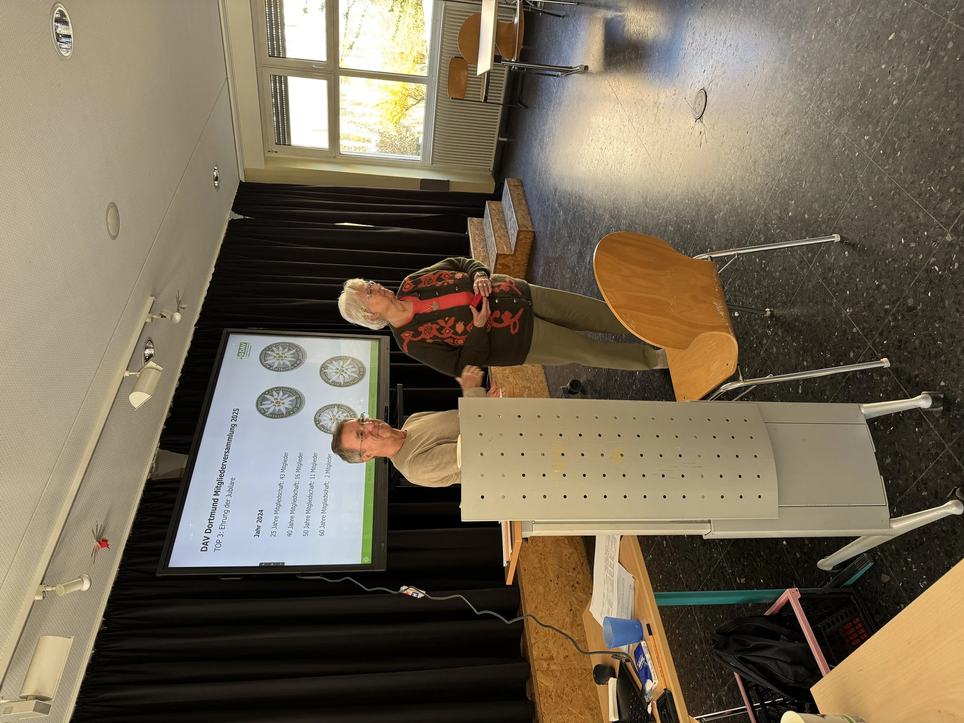 Eine Frau und ein Mann stehen auf der Bühne der Mitgliederversammlung und präsentieren Informationen zur Vereinsmitgliedschaft. | © DAV Dortmund